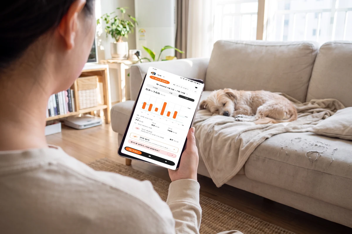 A person checking records on a phone beside a dog resting on the sofa, a scene of looking at resting respiratory rate and activity trends while caring for a dog with heart disease